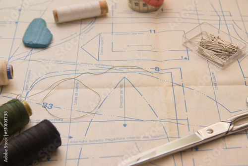 Needles, threads of different colors and scissors cut on a pattern printed on paper. Copy space
