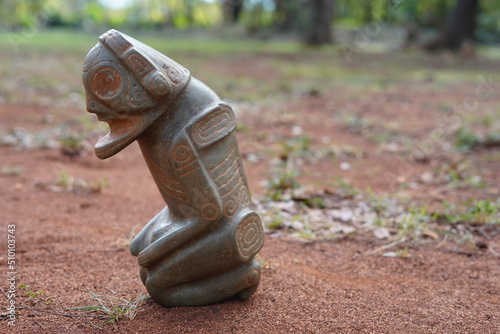 Taino Antique Stone Cemi Idol God Figure standing over red dirt on the ground, close up. Taino Mythology. photo