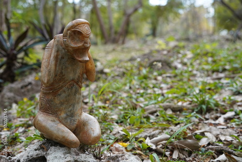 Taino Antique Stone Cemi Idol God Figure standing on rocks on the ground, close up. Taino Mythology. photo