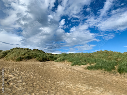 Sand dunes and sea grass tussocks. Summer in England. Creative photograph of sand dunes against a blue sky with clouds. Camber Sands, East Sussex along English Channel.
