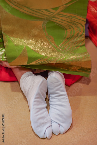 Close up on the backside of a Japanese maiko or geisha woman's feet wearing traditional white socks called tabi worn with thongs footwear such as geta with a long embroidered obi belt on a kimono. photo