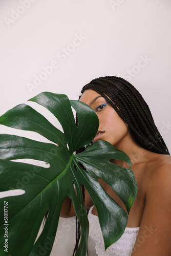 beautiful dark-skinned girl in a white strapless pope on a white background with a large green leaf of a plant photo