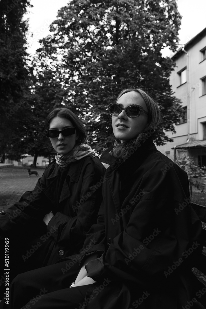 Stylish girls in coats and glasses are sitting in the park Stylish girls in coats and glasses are sitting in the park