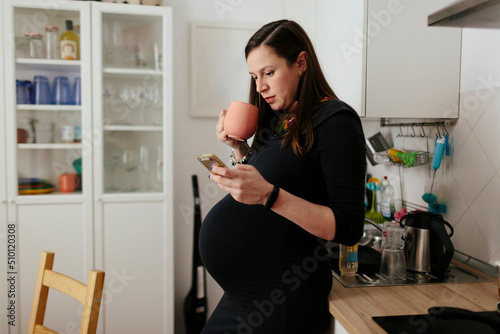 Pregnant woman having breakfast at home while checking her phone photo