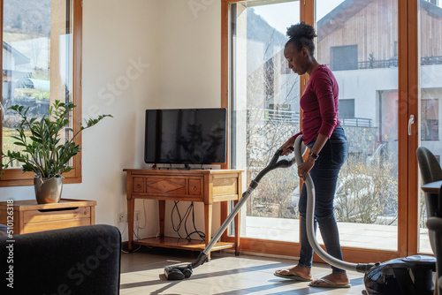 woman hoovering floor at home using vacuum cleaner photo