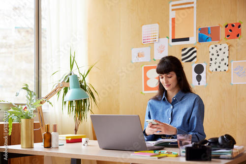 Woman using laptop at desk with laptop in creative room