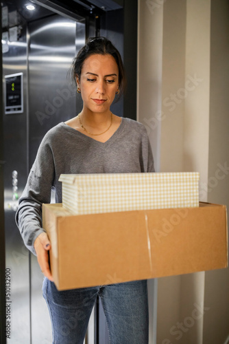 young woman carrying a cardboard box getting out of the elevator photo
