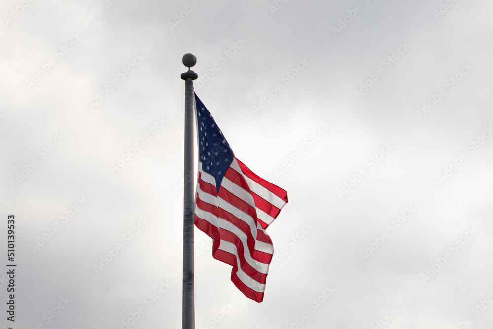American flag on a flagpole with a cloudy sky in the background American flag on a flagpole with a cloudy sky in the background