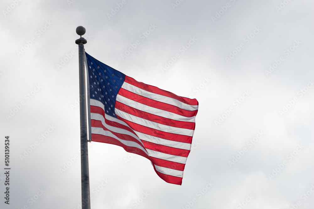 American flag blowing in the wind on a flagpole with a cloudy sky in the background