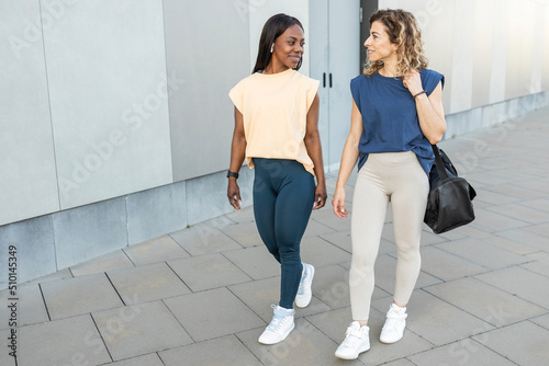 two multiracial women walking together in sportswear through the city