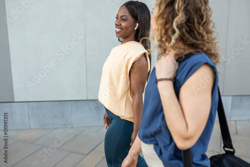 two multiracial women walking together in sportswear through the city