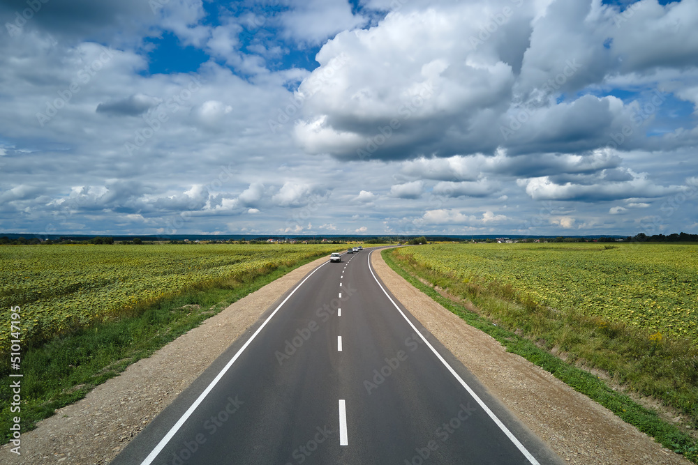 Aerial view of intercity road between green agricultural fields with fast driving cars. Top view from drone of highway traffic Aerial view of intercity road between green agricultural fields with fast driving cars. Top view from drone of highway traffic