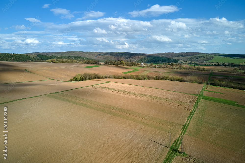 Aerial view of plowed agricultural fields with cultivated fertile soil prepared for planting crops between green woods in spring