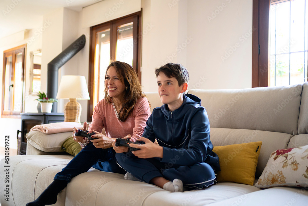 Cheerful boy with mother playing videogame on sofa