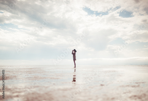 Woman silhouette using binoculars on empty beach photo