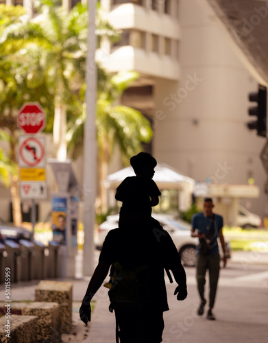 people walking on the street father carrying son on shoulders unrecognizable silhouette
