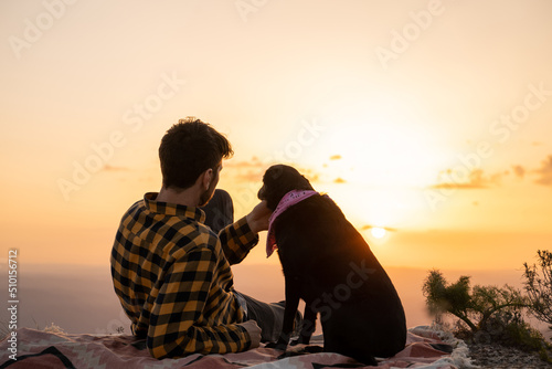 Man and dog sitting on nature at sunset looking at the view photo