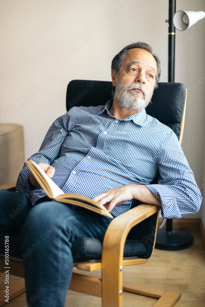 Serious bearded man reading a book in an armchair Serious bearded man reading a book in an armchair