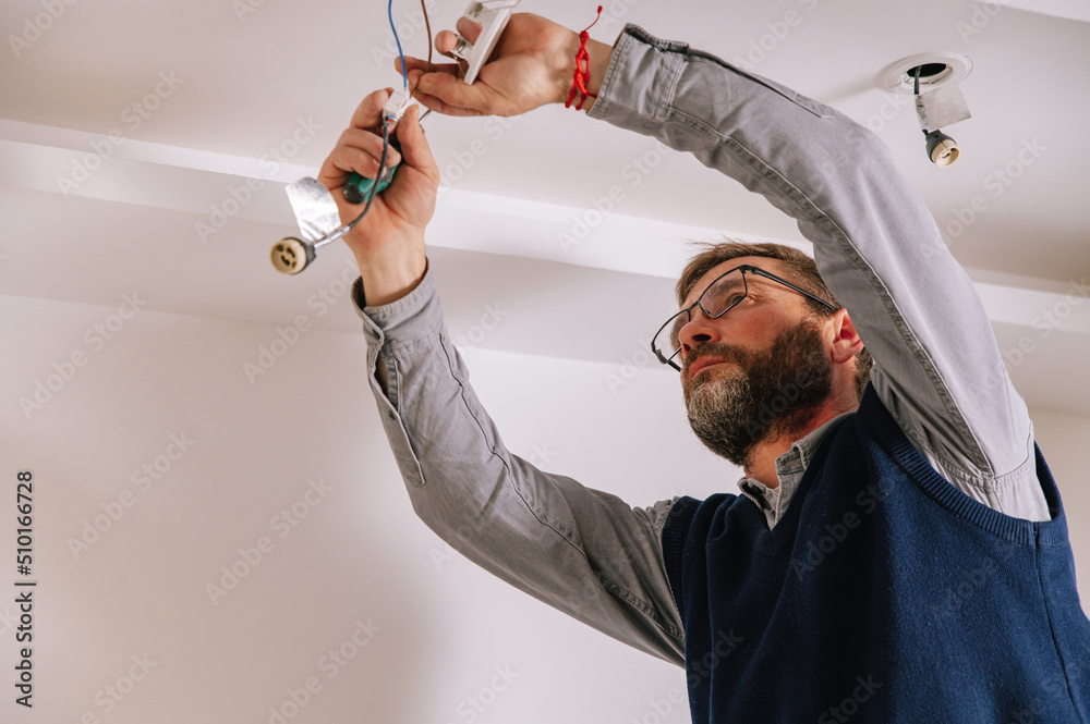 © David Prado/Stocksy - Male electrician installing ceiling illumination © David Prado/Stocksy - Male electrician installing ceiling illumination