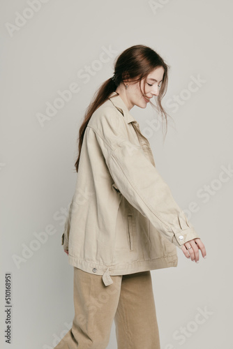 Young joyful woman in a beige jacket runs on a gray background