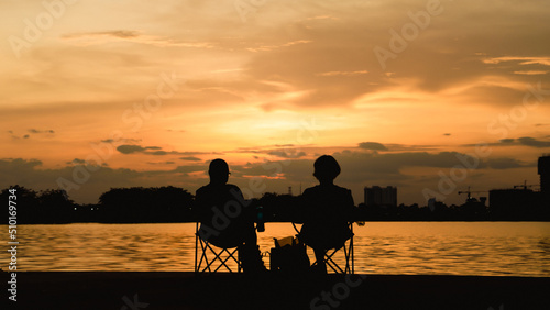 Happy Asian seniors couple enjoying Silhouette beautiful sunset view at the Thatlunag lake in Vientiane city, Laos. Retirement vacation concept.