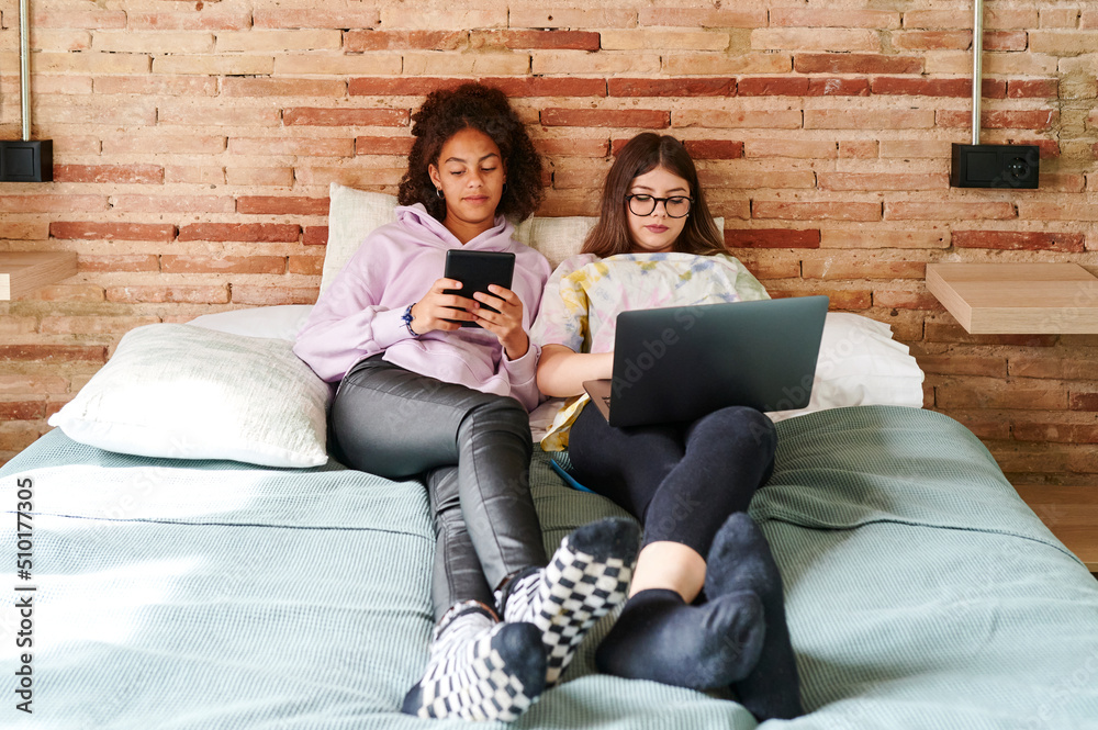Teen girls using different devices on a bed