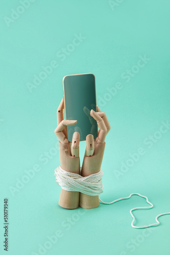 Wooden doll's hands tied with rope hold a smartphone. photo