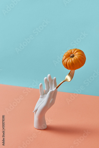 Mannequin hand holds fork with ripe pumpkin.