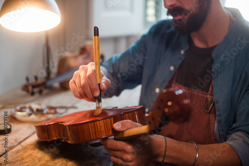 Unrecognisable luthier varnishing a violin photo