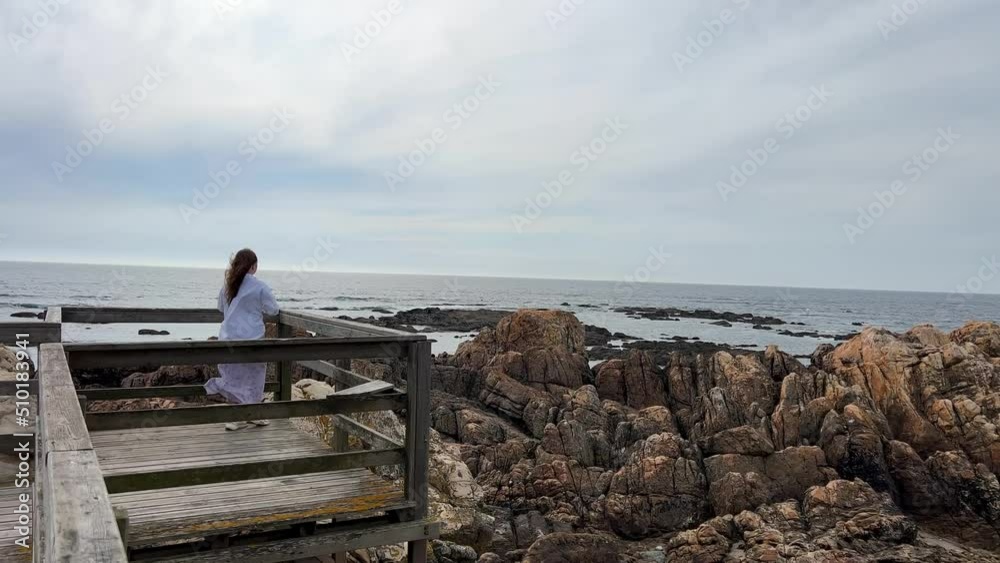 the girl is walking against the backdrop of the Atlantic Ocean, her hair is developing. She is dressed in a white jacket. The weather is cold. veterans. High quality 4k footage