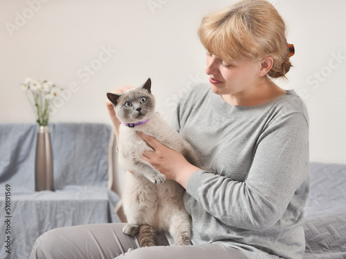 Joyful woman sitting on sofa indoors holding cat