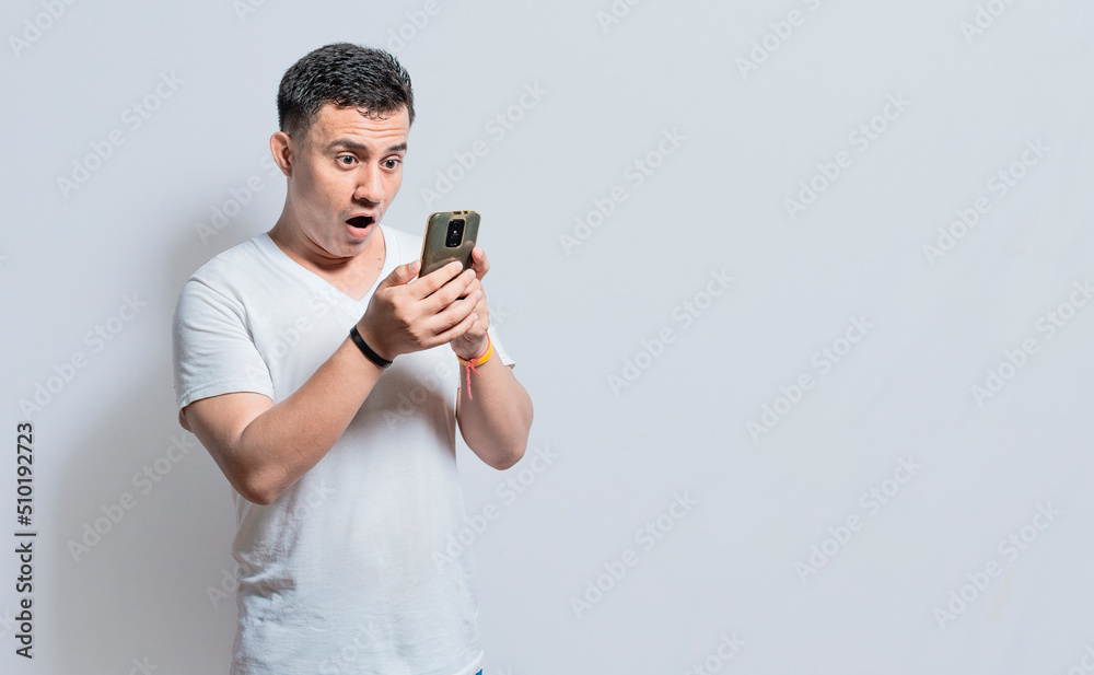 Handsome man with surprised expression with his phone in his hand, An astonished person with his cell phone on isolated background Handsome man with surprised expression with his phone in his hand, An astonished person with his cell phone on isolated background