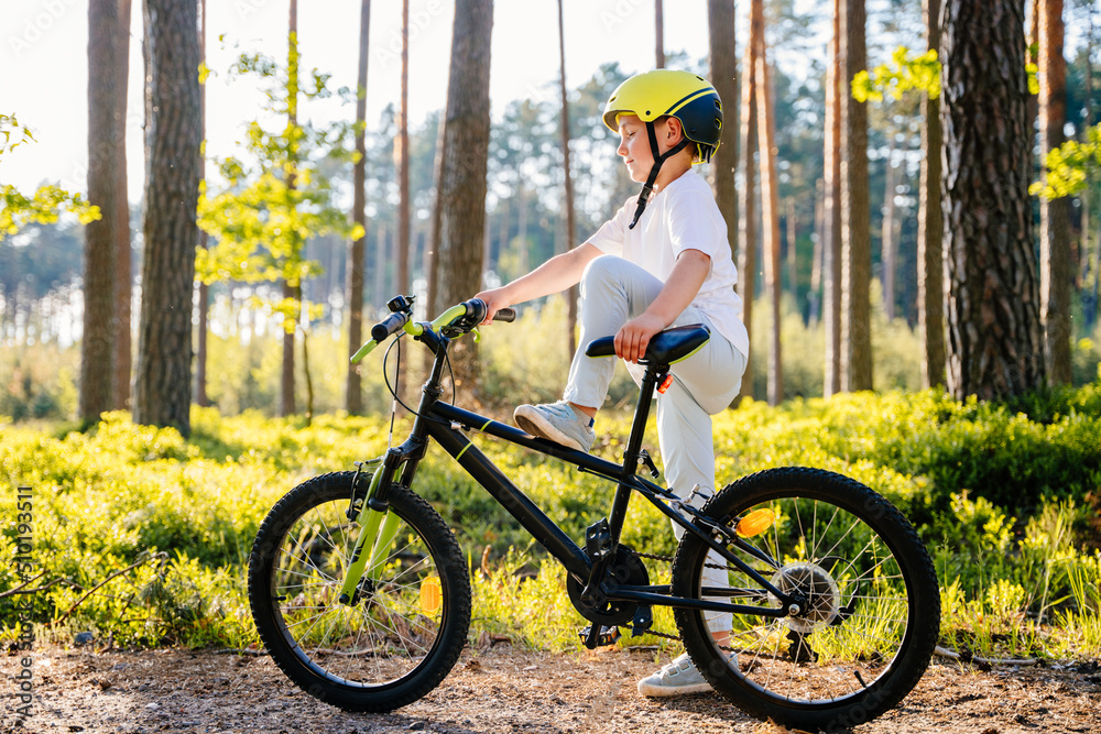 Obraz premium Cute handsome caucasian boy in helmet enjoying riding bike. Child in summer forest learn to balance in bicycle. Summer vacation for inquisitive kid in forest.