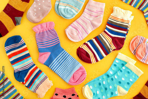 Colorful socks on a yellow background. Clothing in the form of multi-colored socks. Socks of different sizes are scattered on the background.
