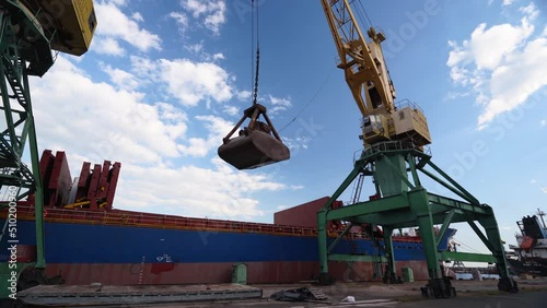 Grain transshipment from container to ship cargo holds with a double rope dual scoop clamshell grab on crane in sea port. Wheat shipment with water transport. Agricultural commodities transportation. photo