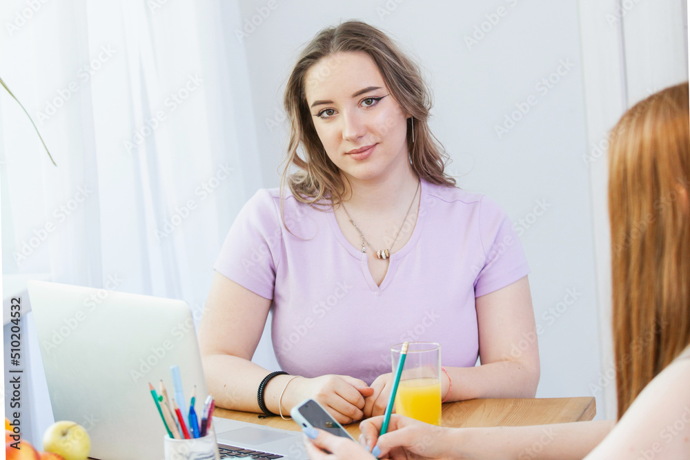 the girls are sitting at the table, eating fruit, drinking juice. They study on a laptop and look at the phone the girls are sitting at the table, eating fruit, drinking juice. They study on a laptop and look at the phone