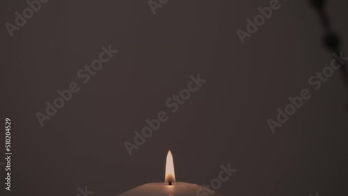 Close-up footage of a candle burning in the dark and a silhouette of a rosary swaying in the background photo