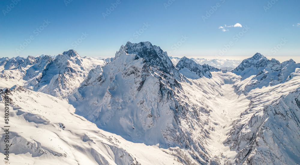 Peaks of the mountain range under the snow above the clouds 