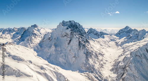 Peaks of the mountain range under the snow above the clouds 