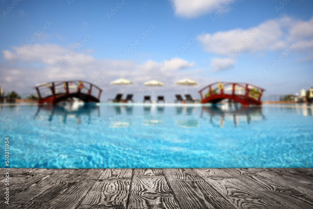 Empty wooden surface near outdoor swimming pool with clear water. Space for design