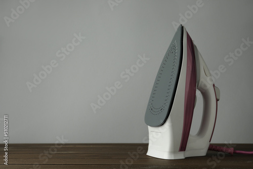 One modern iron on wooden table against light grey background, space for text. Home appliance