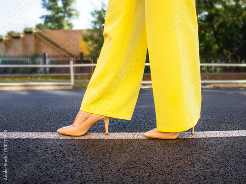 female business style,women's legs in beige high-heeled shoes and bright yellow trousers ,
women's legs in beige high-heeled shoes and bright yellow trousers walk on the asphalt ,selective focus