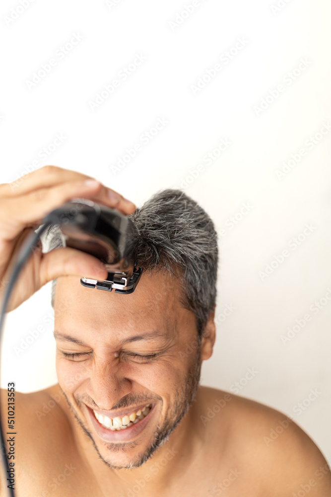 Handsome gray-haired man is cutting hair himself with an electric hair clipper. Handsome gray-haired man is cutting hair himself with an electric hair clipper.