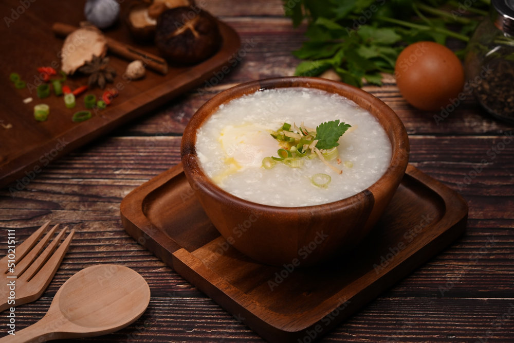 Rice porridge or congee with soft boiled egg, slice ginger and slice scallion topping on wooden table Rice porridge or congee with soft boiled egg, slice ginger and slice scallion topping on wooden table