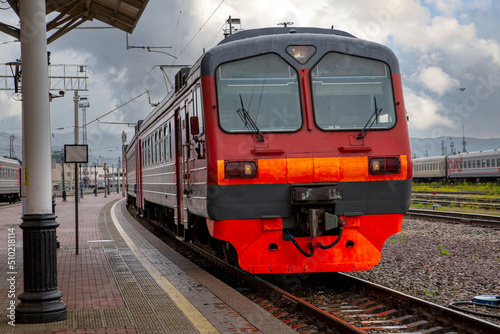 A bright red train pulls up to the platform of the railway station in the city. Passenger Transportation.