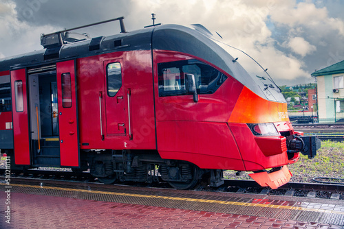 A bright red train stands on the platform of the railway station in the city. Passenger Transportation.