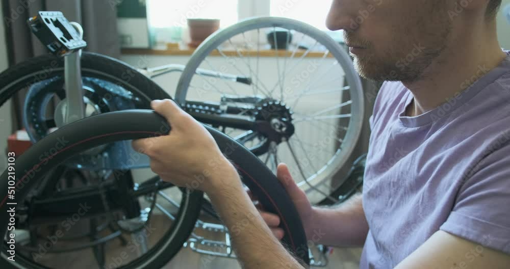 man holds a bicycle camera inner tube in his hands, shows taped punctures on it. Home bicycle workshop with a master. Close-up, disassembled bike in the background. man holds a bicycle camera inner tube in his hands, shows taped punctures on it. Home bicycle workshop with a master. Close-up, disassembled bike in the background.