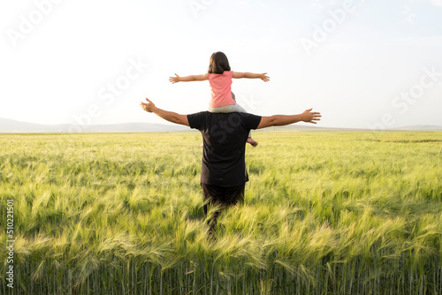 Farmer father, daughter plays on shoulders of farmer father. Happy child and father playing in the wheat field. Father's Day concept idea photo with copy space. © Designerant
