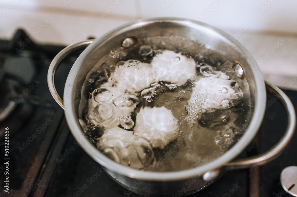 Chicken white eggs are boiled in boiling water in a metal saucepan. Chicken white eggs are boiled in boiling water in a metal saucepan.