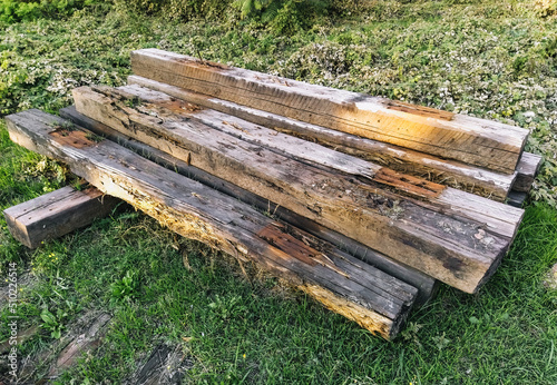 Old, used long wooden sleepers for railway repairs are scattered carelessly, lie on green grass for garbage, recycling. Preparatory work.